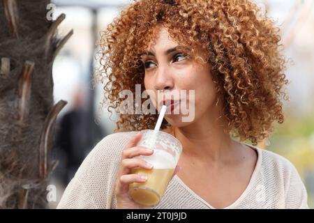 Portrait d'une femme aux cheveux bouclés buvant en plein air dans un pays exotique Banque D'Images