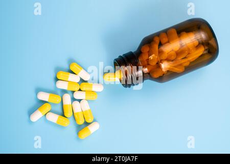 Pilules blanches et jaunes éparpillées près de la bouteille ouverte sur fond bleu. Concept de traitement médical avec des médicaments, des vitamines ou des suppléments dans Banque D'Images