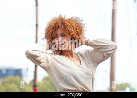 portrait d'une femme en chandail blanc tenant ses cheveux bouclés Banque D'Images