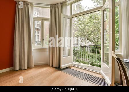 une chambre avec des murs rouges et des rideaux blancs sur les fenêtres donnant sur un patio extérieur qui a du parquet Banque D'Images