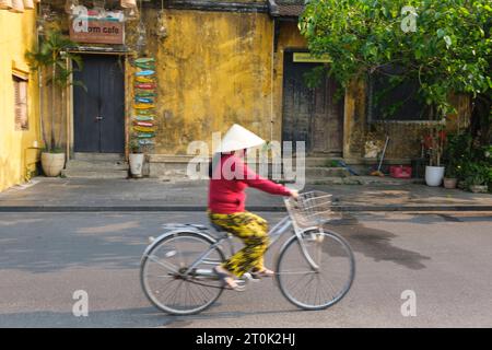 Hoi an, Vietnam. Scène de rue, Femme à vélo, tôt le matin. Banque D'Images