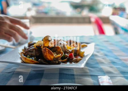 Une assiette de palourdes cuites dans une sauce piment et ail aux haricots noirs dans un restaurant de fruits de mer cantonais le long de Cheung Chau Pier à Hong Kong Banque D'Images