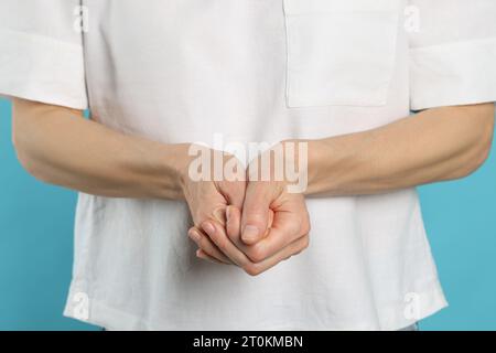 Femme craquant ses jointures sur fond turquoise, closeup. Mauvaise habitude Banque D'Images