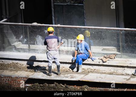 Par une journée ensoleillée, les travailleurs de la construction prennent une pause à côté du bâtiment en construction. Banque D'Images