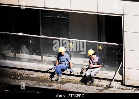 Par une journée ensoleillée, les travailleurs de la construction prennent une pause à côté du bâtiment en construction. Banque D'Images