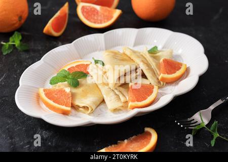 Crêpe française traditionnelle Suzette avec sauce à l'orange. Fines crêpes avec tranche d'orange fraîche sur plaque en céramique ovale. Banque D'Images