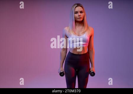 Photo de sportswoman aux cheveux clairs et confiants faisant des exercices avec de petits haltères fond isolé, temps libre, temps libre, passe-temps, mode de vie. cop Banque D'Images