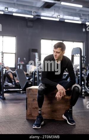 jeune bel homme brunette en vêtements de sport noir a du repos après un entraînement dur, photo pleine longueur. repos. le gars prend une pause Banque D'Images