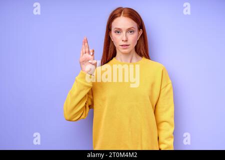 Belle femme rousse démontrant lettre F symbole de langue des signes pour l'humain sourd avec fond bleu. isolé Banque D'Images