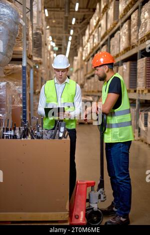 deux gestionnaires d'entrepôt marchant dans un grand centre de distribution d'entrepôt discutant de l'augmentation de la productivité. bon travail d'équipe, des hommes habillés en wor Banque D'Images