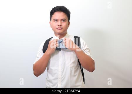 Lycéen indonésien portant un uniforme de chemise blanche avec une cravate grise ajustant sa cravate. Image isolée sur fond blanc Banque D'Images