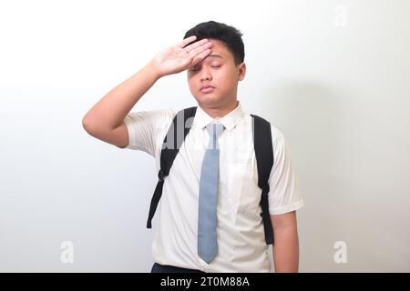 Lycéen indonésien portant un uniforme de chemise blanche avec cravate grise souffrant de maux de tête et tenant les mains sur le front. Image isolée sur wh Banque D'Images