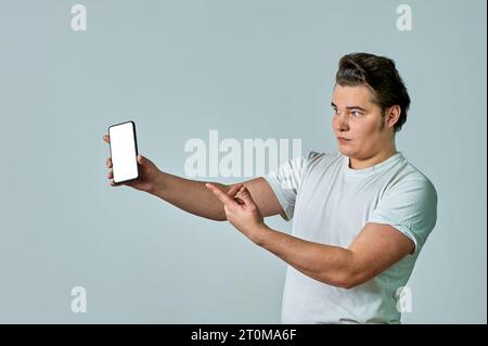 Un homme à bout de bras montre un écran de téléphone sur fond gris, maquette Banque D'Images