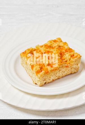 tranche carrée de gâteau de pêche sur assiette blanche sur table en bois blanc, vue verticale, gros plan Banque D'Images