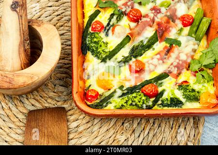 Asperges enveloppées de bacon, cuites avec des tomates, du brocoli et du fromage. Délicieuse cocotte maison Banque D'Images