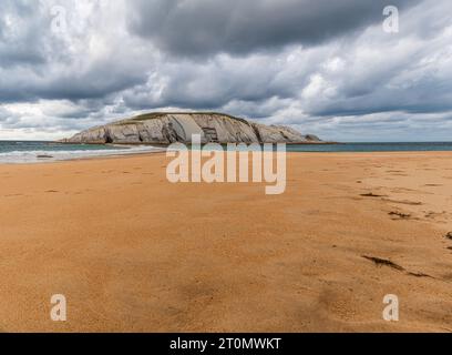 Vue panoramique de Isla del Castro avec plage de sable de Covachos, Santander, Cantabrie, Espagne. Île rocheuse et broche sablonneuse par jour nuageux de mauvaise humeur Banque D'Images