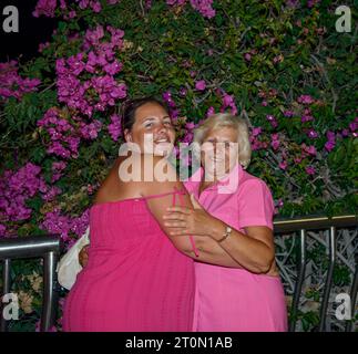 Mère et fille dans des robes rouge vif sont serrées près du buisson bougainvilliers sur la nuit 5th Centennial Avenue, Puerto de Santiago, Tenerife. Banque D'Images