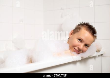 Dans la baignoire chaude remplie de bulles, une femme d'âge moyen se détend. Le bonheur brille à travers son visage Banque D'Images