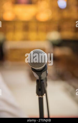 Microphone au premier plan prêt à être utilisé à l'intérieur d'une église ou d'un espace religieux. Fond d'église flou. Banque D'Images