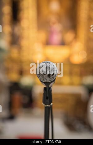 Microphone au premier plan prêt à être utilisé à l'intérieur d'une église ou d'un espace religieux. Fond d'église flou. Banque D'Images