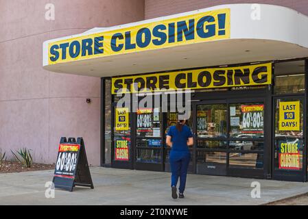 Entrée du magasin avec banderoles de fermeture du magasin et affiches annonçant les remises des derniers jours avec un client entrant dans le magasin. Banque D'Images