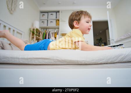 L'enfant joue dangereusement au bord du lit, risquant de tomber. Enfant âgé de deux ans (garçon de deux ans) Banque D'Images