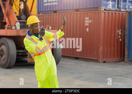 Le docker masculin africain contrôle le chargement de la cargaison de conteneurs au chantier naval de conteneurs d'entrepôt. Employé du personnel maritime et du transporteur. opérateur de chargement de cargaison s Banque D'Images