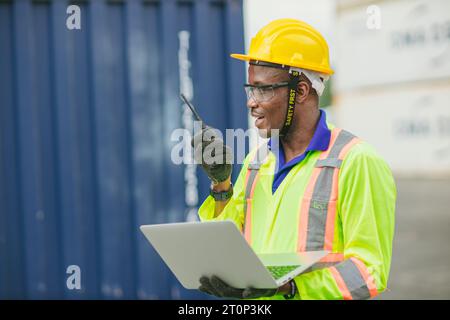 Le docker masculin africain contrôle le chargement de la cargaison de conteneurs au chantier naval de conteneurs d'entrepôt. Employé du personnel maritime et du transporteur. opérateur de chargement de cargaison s Banque D'Images