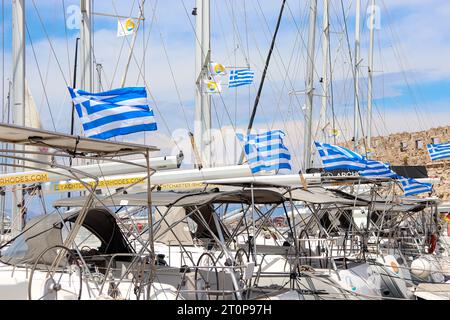 Rangée d'ouvert dans le vent drapeau national de la Grèce accroché sur les bateaux de yacht amarrés le long du port de Mandraki Banque D'Images