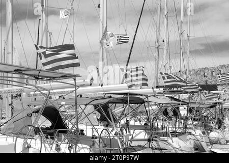 Rangée d'ouvert dans le vent drapeau national de la Grèce accroché sur les bateaux de yacht amarrés le long du port de Mandraki en noir et blanc Banque D'Images