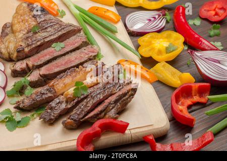 Steak de bœuf marbré moyen rare avec des légumes sur une planche à découper en bois. Viande fraîche grillée. Source naturelle de protéines. Vue de dessus. Gros plan Banque D'Images