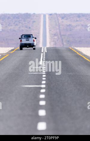 White Toyoya Hilux pick-up camion conduisant le long d'une très droit et long la route goudronnée à travers le désert du Kalahari, en Namibie Banque D'Images