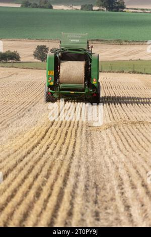 Ramasseuse-presse McHale dans un champ d'orge tronqué produisant une balle ronde de paille vue de l'arrière Banque D'Images