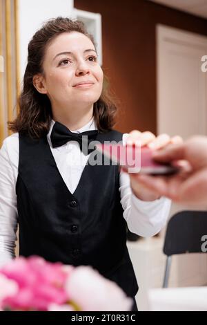 Le concierge féminin accueille et aide les voyageurs âgés, vérifie les pièces d'identité pour l'enregistrement. À la réception, le réceptionniste de l'hôtel reçoit le passeport d'un touriste retraité pour vérification. Banque D'Images