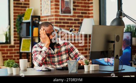 Employé fatigué épuisé après une nuit sans sommeil essayant de rester éveillé tout en travaillant à distance sur l'ordinateur. Télétravailleur surchargé stressé souffrant de maux de tête, luttant pour se concentrer Banque D'Images