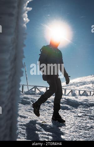 Un randonneur solitaire en vêtements chauds, dans le froid hivernal marche sur la montagne gelée, par jour ensoleillé avec ciel bleu clair et vent fort Banque D'Images