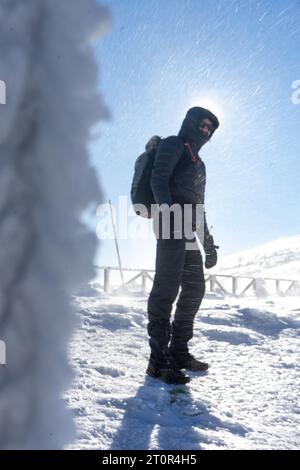 Un randonneur solitaire en vêtements chauds, dans le froid hivernal marche sur la montagne gelée, par jour ensoleillé avec ciel bleu clair et vent fort Banque D'Images