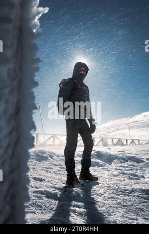 Un randonneur solitaire en vêtements chauds, dans le froid hivernal marche sur la montagne gelée, par jour ensoleillé avec ciel bleu clair et vent fort Banque D'Images