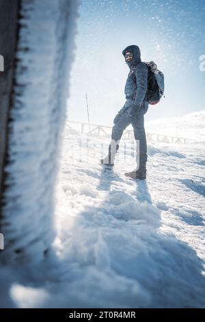 Un randonneur solitaire en vêtements chauds, dans le froid hivernal marche sur la montagne gelée, par jour ensoleillé avec ciel bleu clair et vent fort Banque D'Images