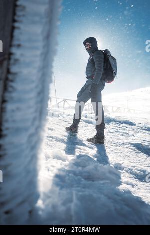 Un randonneur solitaire en vêtements chauds, dans le froid hivernal marche sur la montagne gelée, par jour ensoleillé avec ciel bleu clair et vent fort Banque D'Images