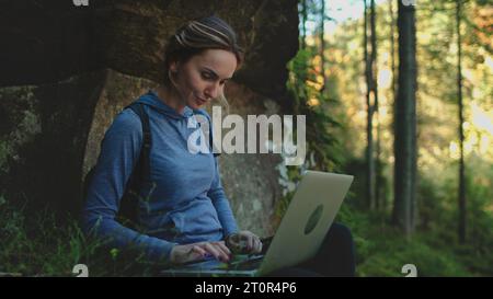 Femme voyageur freelance travaillent en ligne à l'aide d'un ordinateur portable et profitant du beau paysage forestier naturel. Nomade numérique travaillant sur un ordinateur portable, spécialiste INFORMATIQUE travaillant à distance travaillant dans la nature avec de l'air frais Banque D'Images