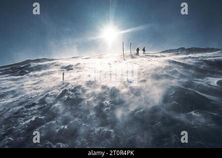 Un randonneur solitaire en vêtements chauds, dans le froid hivernal marche sur la montagne gelée, par jour ensoleillé avec ciel bleu clair et vent fort Banque D'Images