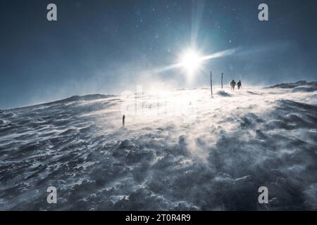 Un randonneur solitaire en vêtements chauds, dans le froid hivernal marche sur la montagne gelée, par jour ensoleillé avec ciel bleu clair et vent fort Banque D'Images