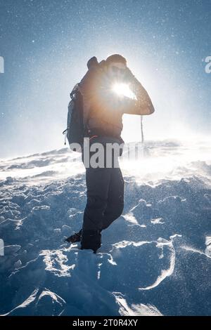 Un randonneur solitaire en vêtements chauds, dans le froid hivernal marche sur la montagne gelée, par jour ensoleillé avec ciel bleu clair et vent fort Banque D'Images