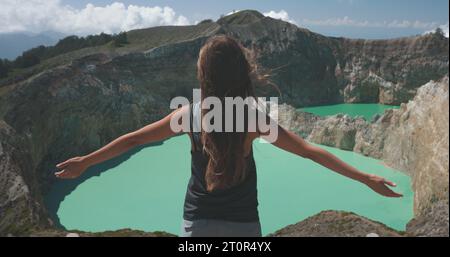 Femme touristique lève les mains au-dessus des lacs de cratère bleu volcanique de Kelimutu. Arrière-plan de la nature. Destination du voyage. Beau paysage sauvage. Vacances d'été exotiques, randonnée, détente. Banque D'Images