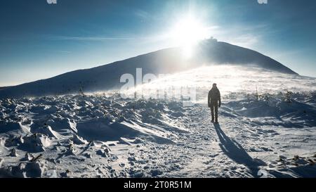 Un randonneur solitaire en vêtements chauds, dans le froid hivernal marche sur la montagne gelée, par jour ensoleillé avec ciel bleu clair et vent fort Banque D'Images