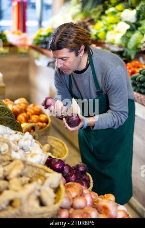 Un travailleur d'épicerie de sexe masculin organise l'oignon rouge et les autres légumes sur le comptoir Banque D'Images