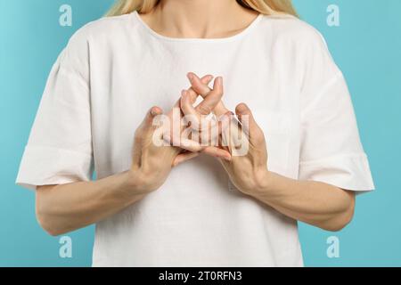 Femme craquant ses jointures sur fond turquoise, closeup. Mauvaise habitude Banque D'Images