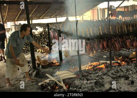 Un travailleur maintient la distribution égale des coques de noix de coco qui sont utilisées comme combustible pour fumer des viandes de thon listao dans une industrie domestique à Bitung, Sulawesi du Nord, en Indonésie. Les contributions des connaissances autochtones à l'innovation technologique offrent un large éventail d'options pour la gestion, entre autres, de la sécurité alimentaire, selon le rapport de 2023 du Groupe d'experts intergouvernemental sur l'évolution du climat (GIEC). Populairement connu sous le nom de cakalang fufu, le thon fumé est considéré comme un aliment indigène exotique et pourrait devenir une solution alternative pour faire face aux impacts du changement climatique sur l’océan. Banque D'Images