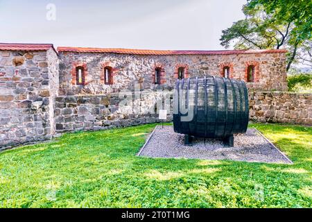 Un fragment du mur d'une ancienne forteresse et un grand tonneau en bois pour le vin dans la ville de Bech, en Pologne. Banque D'Images